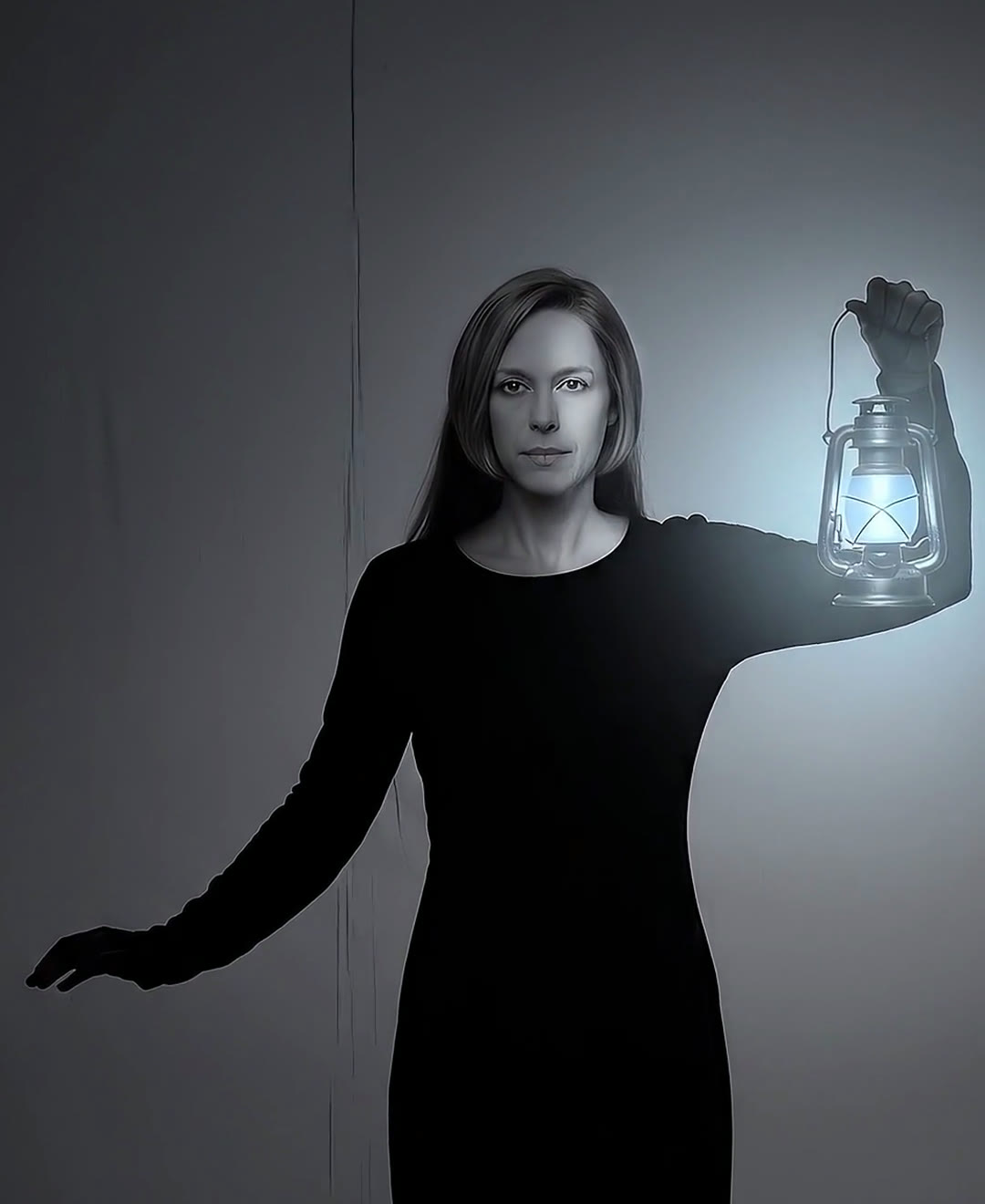 A woman in a long black dress holds up a lantern glowing pale blue, its light showing one side of her face against a dim wall
